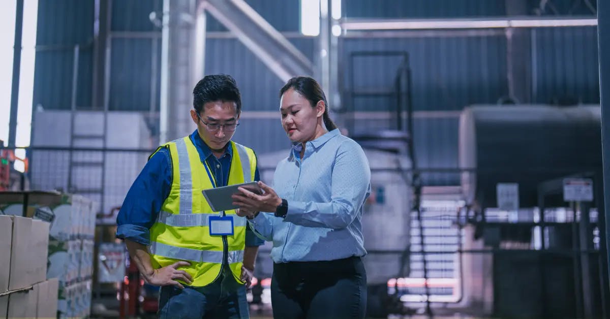 Two professionals conducting a manufacturing process audit in an industrial setting, reviewing data on a tablet